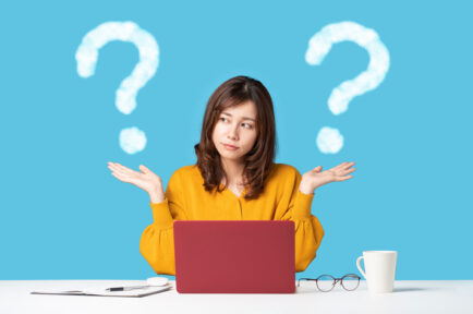 Young woman in front of laptop holding up two graphic question marks to depict the comparison on two things