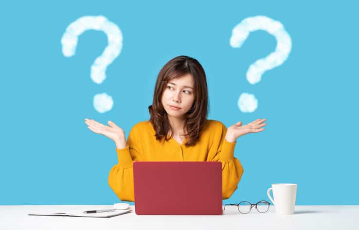 Young woman in front of laptop holding up two graphic question marks to depict the comparison on two things